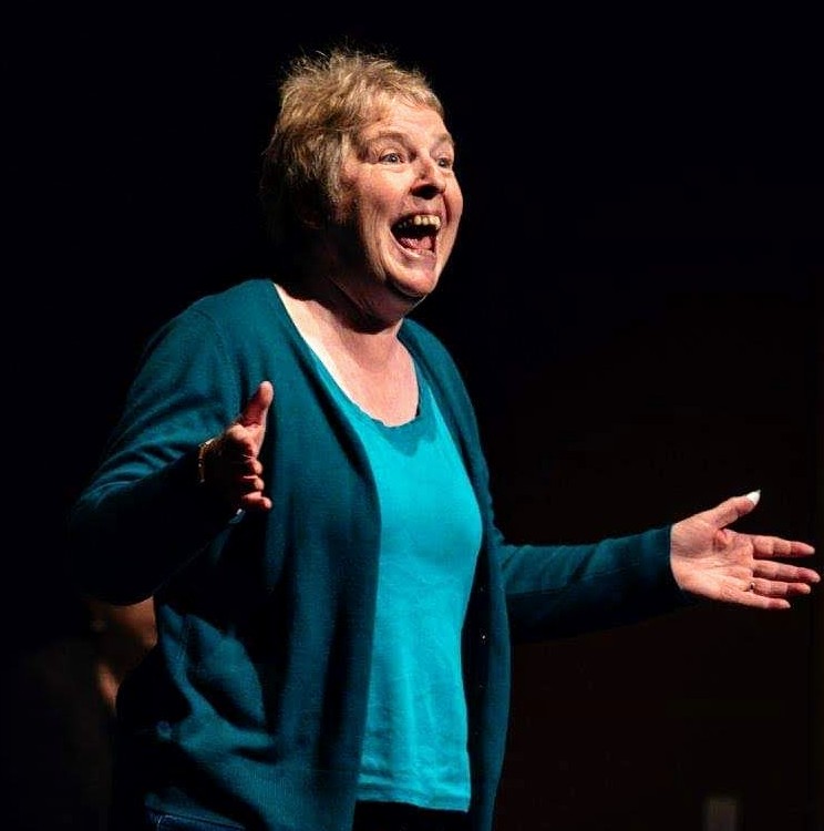 Betty smiling with her arms outstretched as she tells a story.