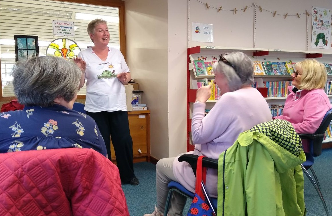 Betty telling stories in a library while listeners smile and watch attentively.